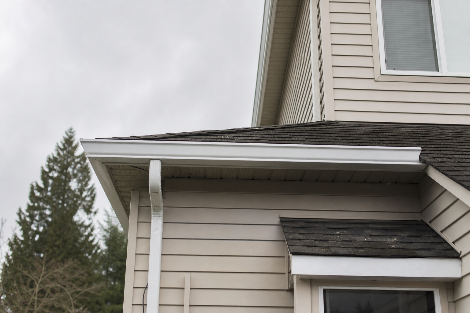 Newly installed white aluminum gutters and downspout along the fascia of a Surrey home